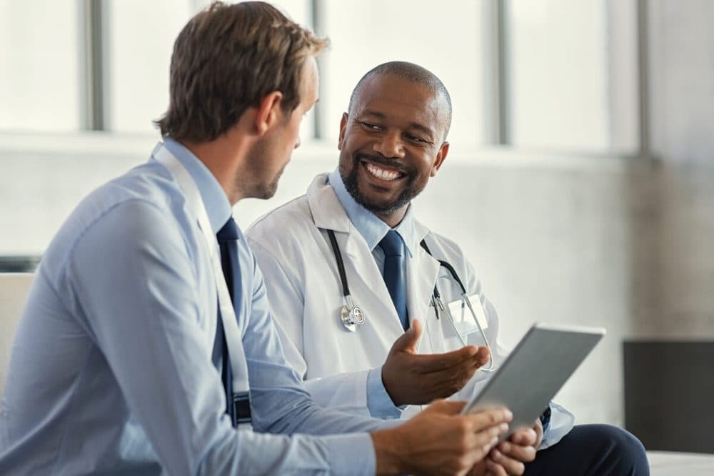 Two colleagues reviewing notes together on a tablet in a consulting room